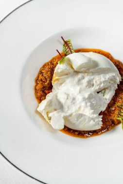 Marullu bufalo mozzarella. Sebze yahnisi, fındık ve şarap sosu. Yemek seramik tabakta yatıyor. Tabak bir bardak beyaz şarap ve çatal bıçak takımının yanında hafif bir masa örtüsünün üzerinde duruyor..