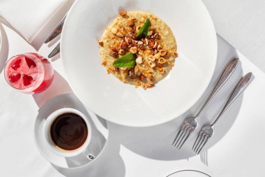 Fındıklı yulaf ezmesi ve hafif seramik tabakta nane yaprakları. Tabak hafif bir masa örtüsünün üzerinde, yanında bir bardak meyve suyu ve bir fincan kahve var..