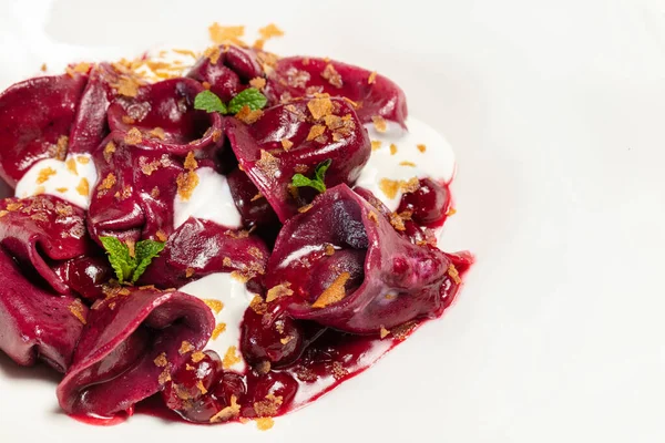 Ukrayna usulü vareniki yemeği, kırmızı hamurdan yapılmış, garganzola peyniri ve mısır gevrekleri hafif kremalı tabakta. Tabak hafif bir masa örtüsünün üzerinde duruyor, yanında bir fincan çay ve çatal bıçak takımı var..