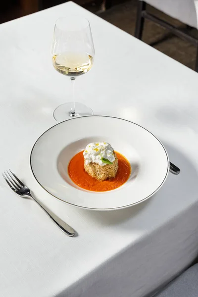 トマトソースのサクサクとしたパンで焼いたナス バジルの葉と軽いセラミックプレートの上にStracciatellaチーズ プレートは 白ワインのガラスの横にある軽いテーブルクロスに立っています — ストック写真