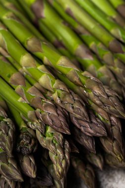 Açık kahverengi arka planda lastik bantla bağlanmış iki taze kuşkonmaz sürüsü..