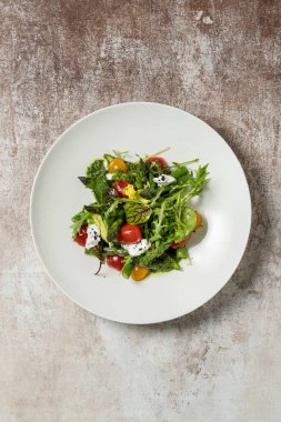 Kuşkonmaz soslu bahar salatası, kırmızı ve sarı kiraz domatesleri, garganzola peyniri, marul karışımı ve pesto soslu mikroçerez. Salata, kumaş arka planında hafif bir seramik tabakta yatıyor..