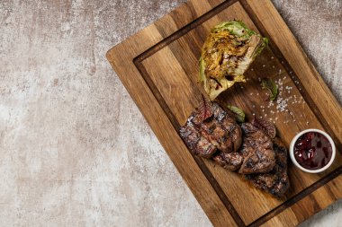 Üç parça fileminyon biftek ızgarada, tahta bir tahtanın üzerinde yatıyor. Yakınlarda balzamik soslu ızgara lahana ve vişne soslu bir kase var. Tahta hafif bir arkaplanda yatıyor.