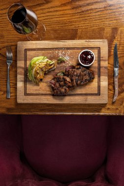Üç parça fileminyon biftek ızgarada, tahta bir tahtanın üzerinde yatıyor. Yakınlarda balzamik soslu ızgara lahana ve vişne soslu bir kase var. Tahta kahverengi bir masada yatıyor..
