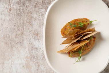 Hafif seramik tabakta patlıcan, paprika ve Ermeni lavaş cipsi ile domates havyarı. Çanak hafif bir arkaplanda duruyor.