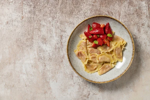 Stock image Vareniki with cottage cheese and strawberries and slices of fresh strawberries on top. The dish lies in a light ceramic plate. The plate stands on a light, fabric background.