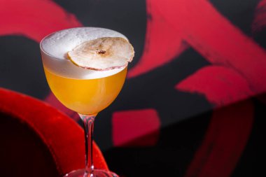 Buzlu, kurumuş armut ve cam köpüklü bir kokteyl boyalı bir duvarın arka planında bir koltuğun üzerinde duruyor.