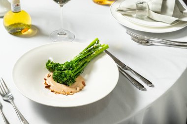 Ceviz soslu ızgara brokoli ve hafif seramik tabakta fıstık. Tabak bir bardak beyaz şarap ve çatal bıçak sehpasının yanında hafif bir masa örtüsünün üzerinde duruyor..