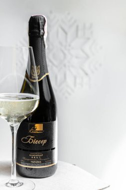 Bir şişe Ukrayna şarabı Kolonist Bisser ahşap bir masanın üzerinde Ukrayna süslemeleri ve bir mücevher ve çiçek çelengi ile beyaz bir duvarın arkasında duruyor..