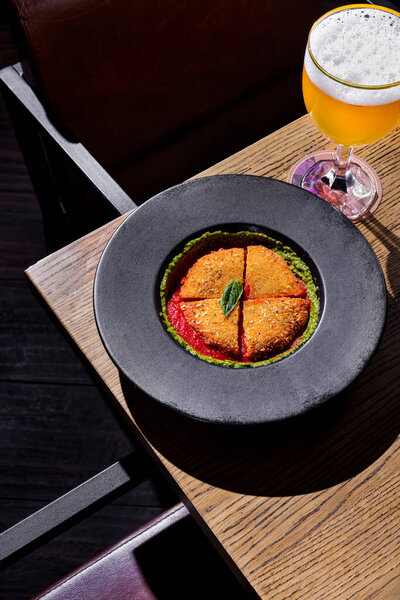 Fried chicken cutlet with basil and pea sauce in a plate standing on the table with a glass of beer