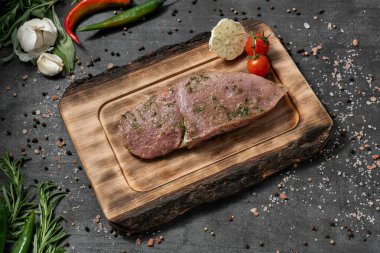 Baharatlı sebze salamuralı domuz filetosu. Açık tahta bir tahtanın üzerinde duruyor. Tabaklar karanlık bir taşın üzerinde duruyor, baharatlar ve bitkiler etrafa saçılmış..