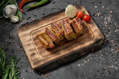 Domuz kaburgası, salamura otlar ve kırmızı biber. Açık tahta bir tahtanın üzerinde duruyor. Tabaklar karanlık bir taşın üzerinde duruyor, baharatlar ve bitkiler etrafa saçılmış..