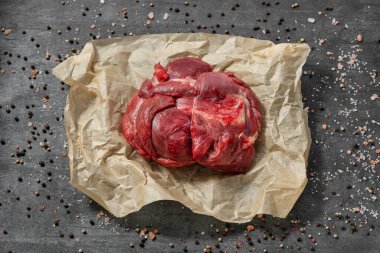 Kağıt üzerinde sığır filetosu, koyu bir taş zemin üzerinde duruyor, tuzlu ve biberli bezelyeler etrafa saçılıyor..