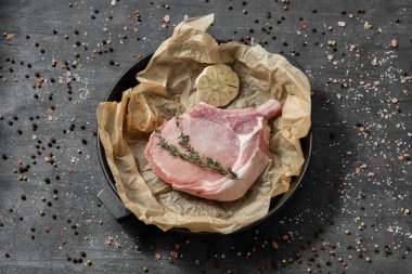 Dökme demir bir tavada, parşömenin üzerindeki domuz eti. Tabaklar karanlık bir taşın üzerinde duruyor, baharatlar ve bitkiler etrafa saçılmış..