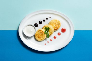 Ekşi kremalı ve hafif seramik tabakta reçelli ev yapımı peynirli peynirli kekler. Plakayı renkli bir kağıda yerleştir.