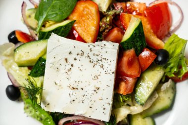 Bir parça peynirli Yunan salatası, zeytinyağı ve seramik bir tabakta İtalyan otları. Plakayı renkli bir kağıda yerleştir.