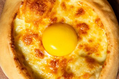 Tekne şeklinde Adjarian Khachapuri, suluguni peyniri ve taze yumurta sarısı. Yiyecek, renkli bir kağıdın üzerinde, ahşap bir tezgahta yatıyor..