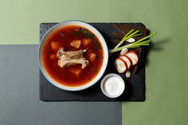 Ukrayna çorbası Borsch, kemiklerinde et ve derin bir tabakta. Siyah ekmekten yapılmış tostlar, domuz yağı, yeşil soğan ve yanında ekşi krema bulunan bir kase. Yemek kağıdın arka planında bir tahtada yatıyor..