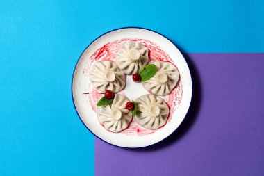 Kirazlı Gürcistan yemeği-tatlı khinkali. Khinkali kiraz sosu ve nane yapraklarıyla seramik bir tabağın üzerinde. Plakayı renkli bir kağıda yerleştir.