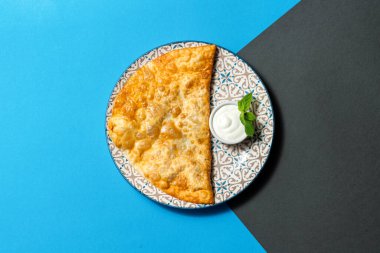 Vişne dolgulu ve üzeri pudra şekerli doğu usulü çeburek. Yakınlarda ekşi kremalı bir seramik kase var. Renkli arka planda seramik tabakta yemek.