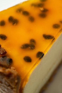 Vanilyalı peynirli kek, turunçgil özü ve tutkulu meyveli jöle. Tatlı yuvarlak bir seramik tabakta, kağıt renkli bir arka planda yatıyor..