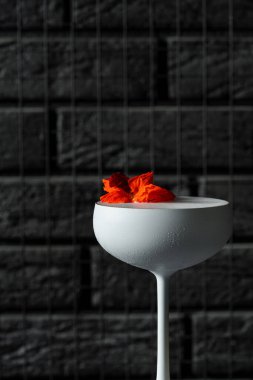 Beyaz cin, limoncello, soda ve çiçeklerle süslenmiş kokteyl. Siyah bar taburesinde beyaz bardakta bir kokteyl..