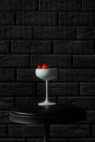 Cocktail with white gin and limoncello, soda and decorated with flowers. A cocktail in a white glass on a black bar stool.