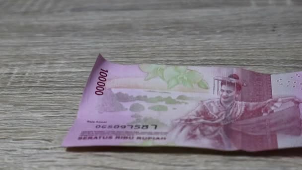 数十万ルピア紙幣が木彫りのテーブルの上に投げ込まれているところで支払いをしている人のビジネスと金融部門のビデオイラスト — ストック動画