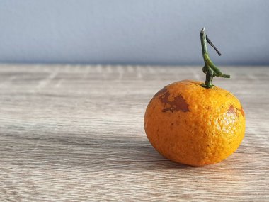 Bu ahşap masadaki küçük bir portakalın fotoğrafı. Bu küçük portakalın yapraksız yeşil bir gövdesi var..