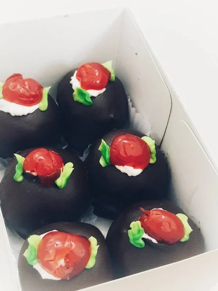 A box of mini black forest cakes, cake with chocolate coating and cherry fruit topping on top. These small shapes are perfect for afternoon snacks with tea.