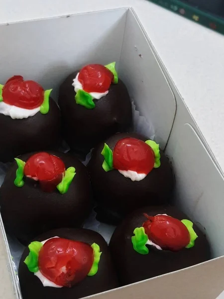 A box of mini black forest cakes, cake with chocolate coating and cherry fruit topping on top. These small shapes are perfect for afternoon snacks with tea.