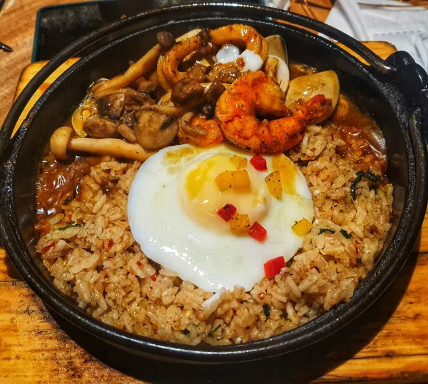Japanese seafood fried rice served on a steel hot plate. This fried rice consists of fried rice itself supplemented with a sunny side up egg, prawns, clams and squid.