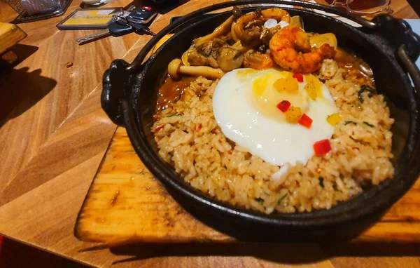 Japanese seafood fried rice served on a steel hot plate. This fried rice consists of fried rice itself supplemented with a sunny side up egg, prawns, clams and squid.