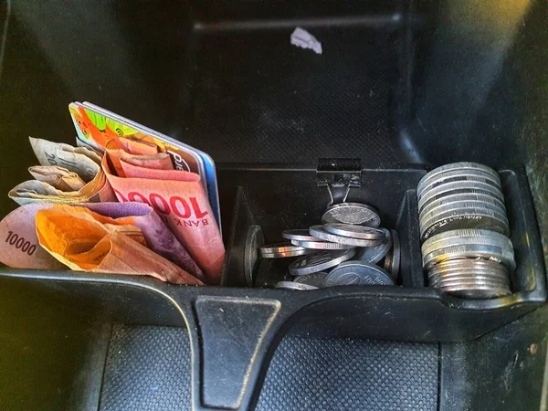 いくつかのルピア硬貨と10万ルピア紙幣と硬貨の場所として機能する車のダッシュボード上に提供されるボックス内の他のお金 — ストック写真