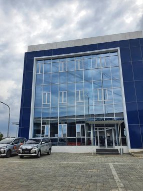 Mavi duvarları olan bir ofis binası ve bulutları yansıtan camdan bir cephe ve gökyüzü çok güzel. Önüne birkaç araba park edilmiş..