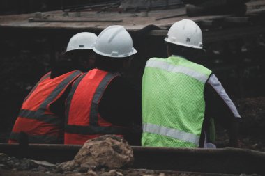 Cakarta, Endonezya Temmuz 2022. Üç inşaat işçisi işten sonra dinlenmek için inşaat sahasının kenarında oturuyorlar, hala kask ve yelek giyiyorlar..