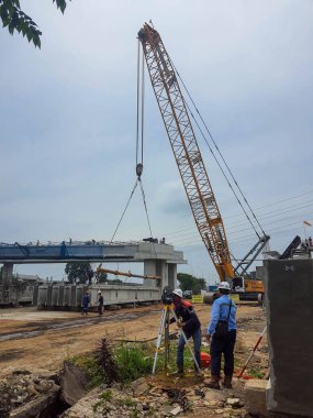 Cakarta, Endonezya Aralık 2022. İki arazi mühendisi inşaat projesi üzerinde çalışıyor. Arkasında kiriş ereksiyonu var..