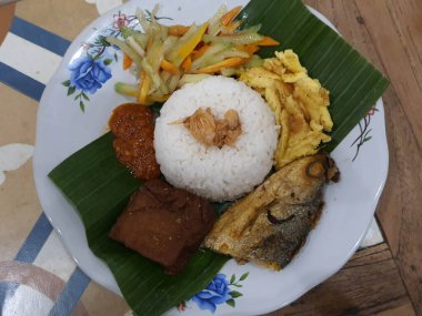 Nasi Kucing 'in bir kısmı kızarmış sütçü balığı başlıklı, tofu, muz yapraklı bir tabakta servis ediliyor. Pirincin üstüne kızarmış soğan serpilmiş. Yendiğinde tadı daha lezzetli olsun diye..