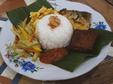 Nasi Kucing 'in bir kısmı kızarmış sütçü balığı başlıklı, tofu, muz yapraklı bir tabakta servis ediliyor. Pirincin üstüne kızarmış soğan serpilmiş. Yendiğinde tadı daha lezzetli olsun diye..
