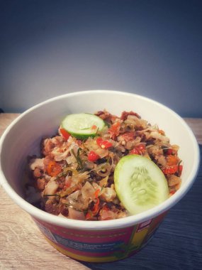 Close up photo of Ayam Geprek Sambal Matah, one of Indonesian specialties. Flour fried chicken is crushed and mixed with sambal matah. Served with rice and cucumber for lalapan.