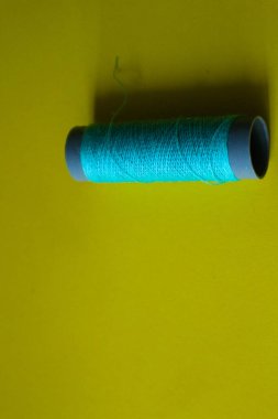 Isolated photo of a ball of light blue thread above and in front of a yellow background. This thread is a bit loose from the reel.