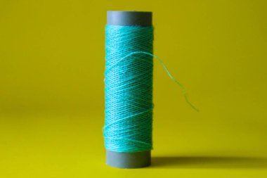 Isolated photo of a ball of light blue thread above and in front of a yellow background. This thread is a bit loose from the reel.