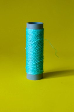 Isolated photo of a ball of light blue thread above and in front of a yellow background. This thread is a bit loose from the reel.
