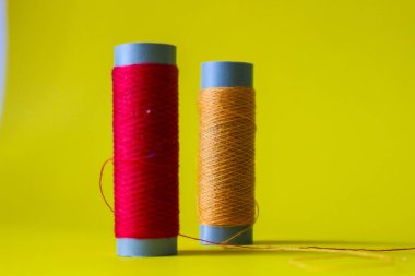 Isolated photo of a roll of red and orange thread above and in front of a yellow background. This thread is a bit loose from the reel.
