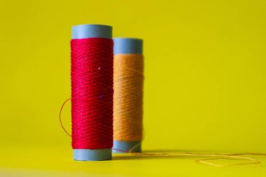 Isolated photo of a roll of red and orange thread above and in front of a yellow background. This thread is a bit loose from the reel.