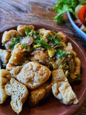 Tahu Gejrot on a clay plate, it is a spicy tofu from Indonesia Made from fried tofu cut into small pieces, served with a thin and watery dressing that is made by blending palm sugar, vinegar and sweet soy sauce and chili