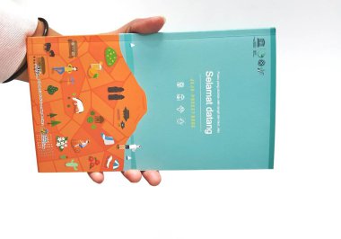 Jakarta, Indonesia in May 2022. A hand is holding a welcome guide book for travelers on vacation on Jeju Island, the JEJU POCKET BOOK. Which contains recommendations for tourist spots, culinary, attractions, tours and various other information.