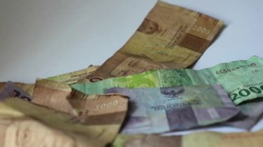Bir elin rupiah kağıdını sayfa sayfa aldığı bir video. Bu paranın çekilmesi kişisel finans, aile mali yönetimi veya tatil tasarrufları ile ilgili resimler için uygundur.