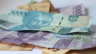 Bir elin rupiah kağıdını sayfa sayfa aldığı bir video. Bu paranın çekilmesi kişisel finans, aile mali yönetimi veya tatil tasarrufları ile ilgili resimler için uygundur.