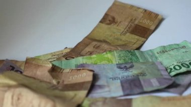 Bir elin rupiah kağıdını sayfa sayfa aldığı bir video. Bu paranın çekilmesi kişisel finans, aile mali yönetimi veya tatil tasarrufları ile ilgili resimler için uygundur.